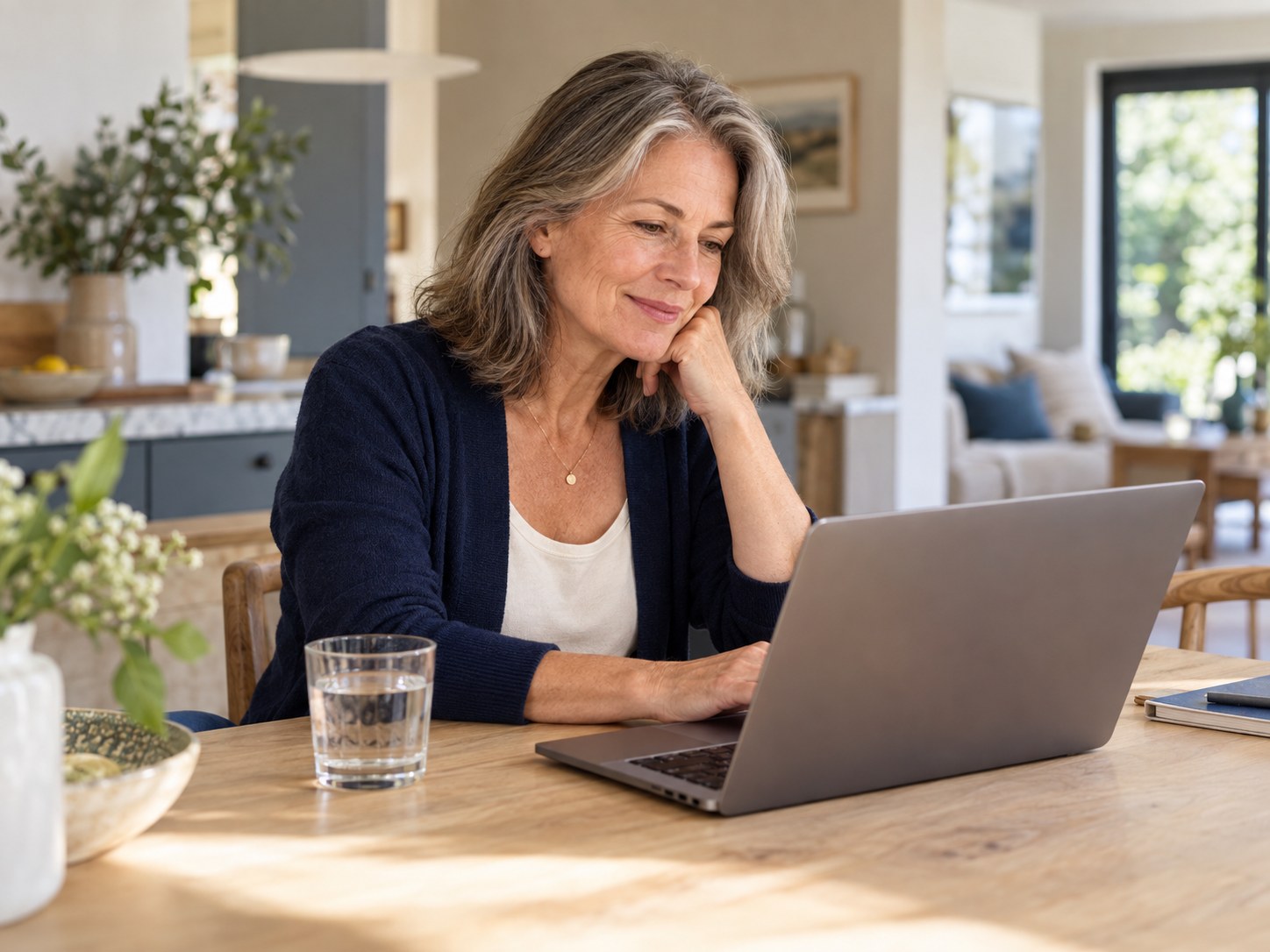 Smiling woman in her fifties at a kitchen table typing a message on her phone